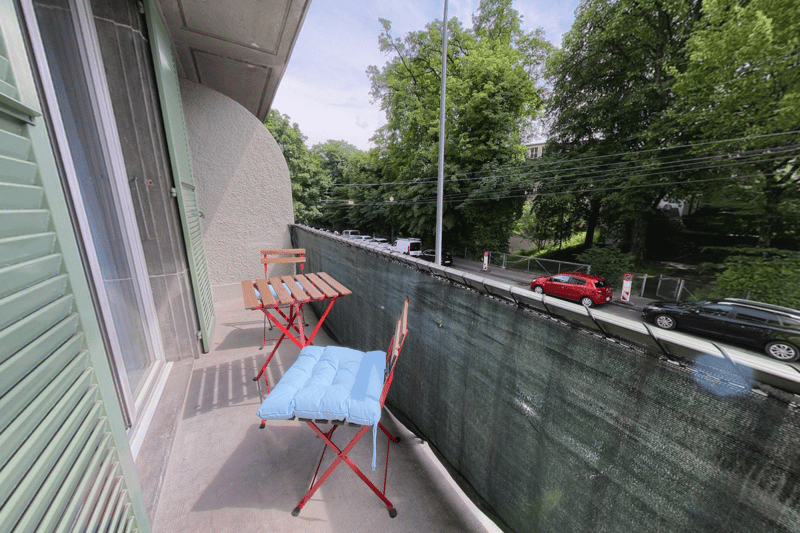 outdoor space with tables and chairs, metal railings, trees and greenery in the background, street view