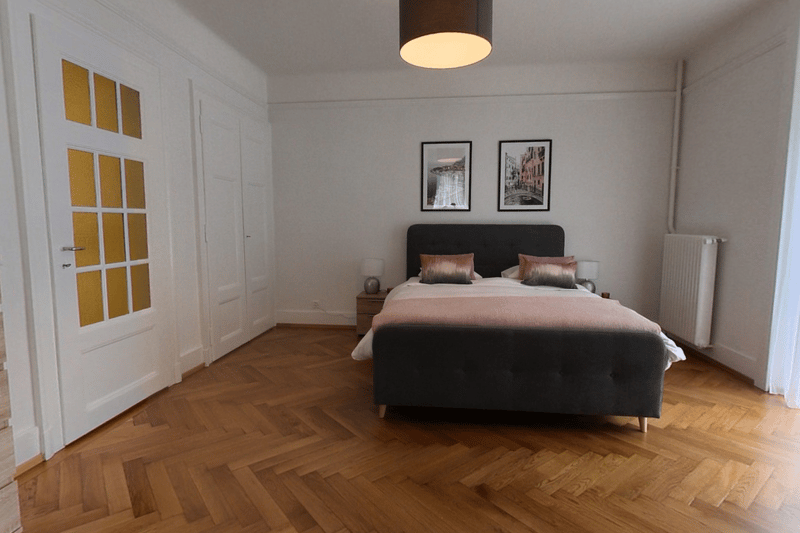 wooden floors, large bed, nightstands with lamps, radiator, picture frames, doors, wooden staircase