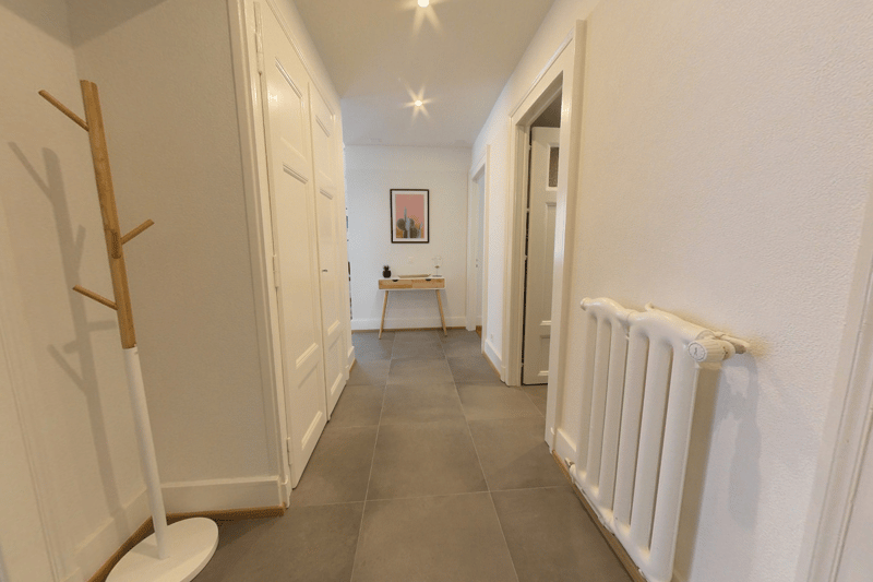Gray tile floor, white walls, wooden coat rack, small table with plant, radiator