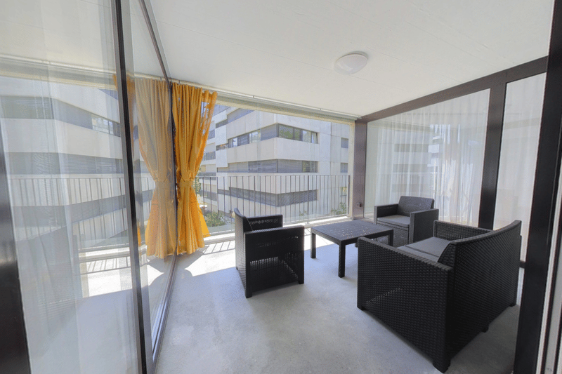 Balcony with glass walls, black wicker furniture, yellow curtains, view of the city