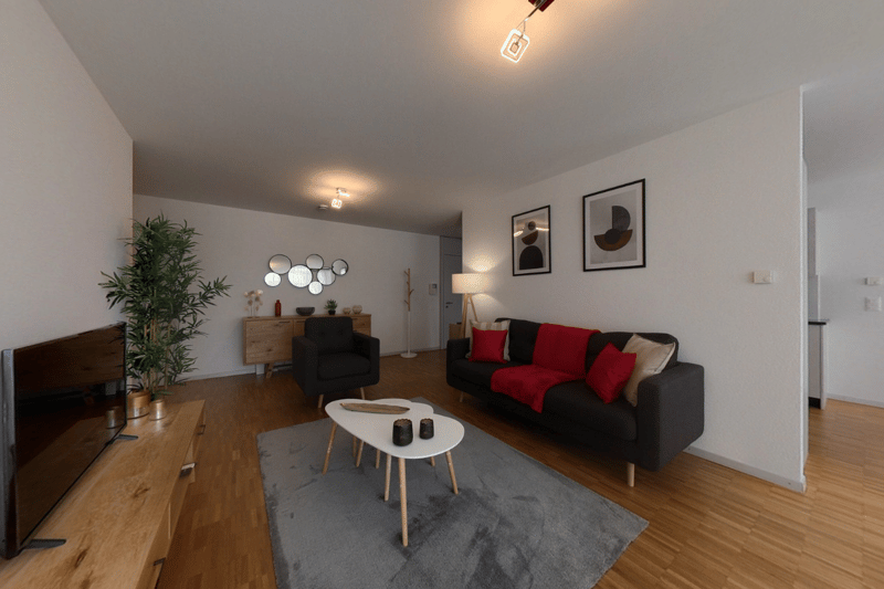 Living room with couch, coffee table, armchair, TV, wooden floor, white walls, plants, and framed pictures.