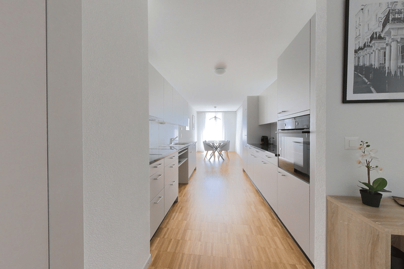 modern kitchen with white cabinets, wooden floor, modern appliances, dining table, picture frame