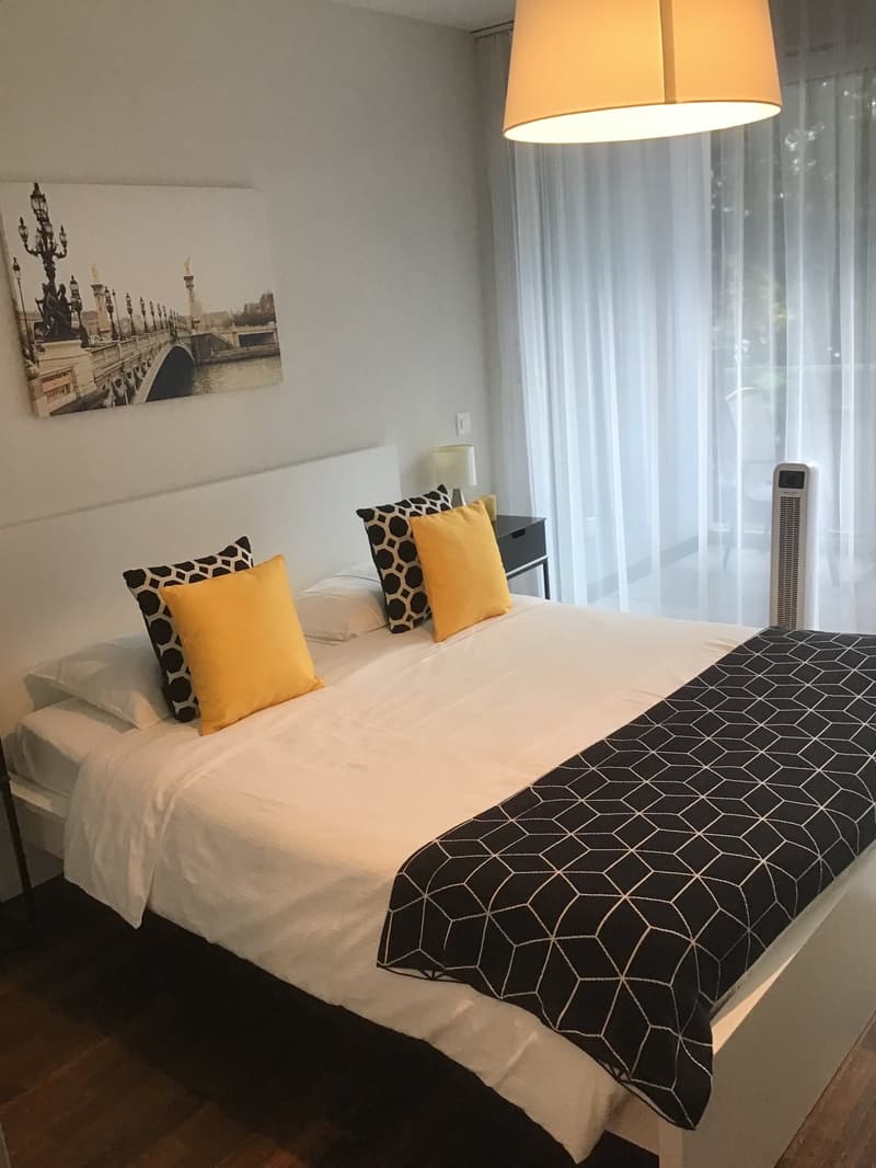 Bedroom with a bed, pillows, blanket, nightstand, lamp, and a painting on the wall