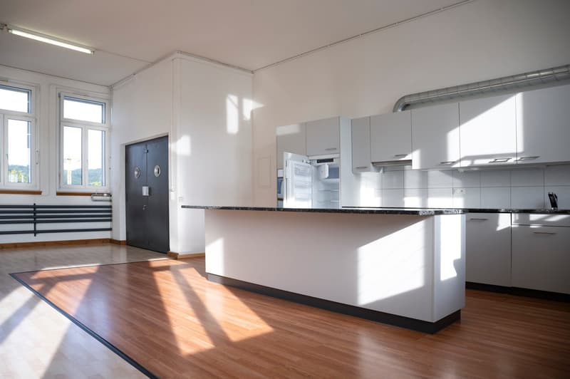 Spacious kitchen with white cabinets, granite countertops, hardwood floors, and large windows providing natural light. The kitchen includes a dishwasher and appears to be part of an open-concept living space.
