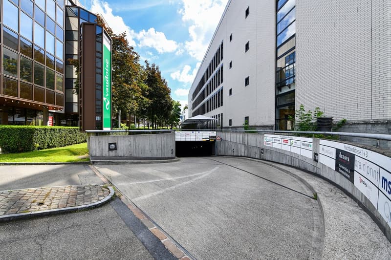 Large commercial building with glass facade, parking entrance, and surrounding landscaping