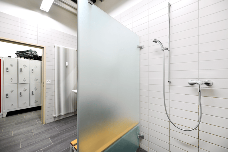 Tiled bathroom with a glass shower enclosure, a shower head, and lockers in the background.