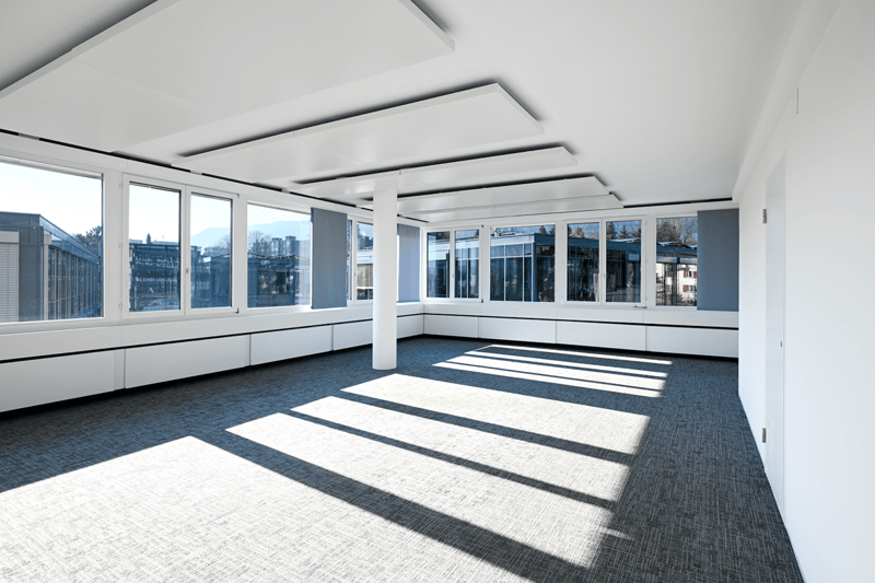 Empty room with white walls, gray carpet, large windows, central column, ceiling panels