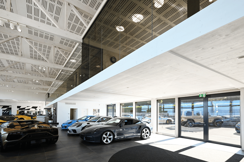 Modern, industrial design car showroom with multiple cars, high ceilings, large windows, polished floors
