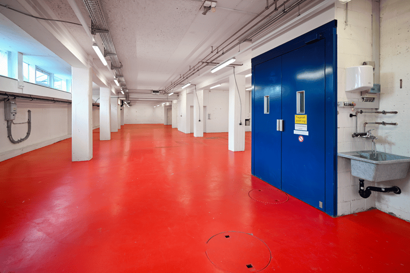 Empty basement, red floor, white ceiling, white columns, blue door, small sink