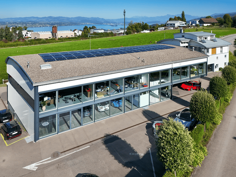Office building, two-story, glass windows, multiple solar panels on the roof, green landscape, parking spaces