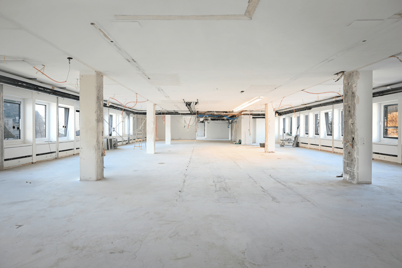 Empty room, unfinished, white walls, concrete floor, ceiling wirings, windows, two pillars.