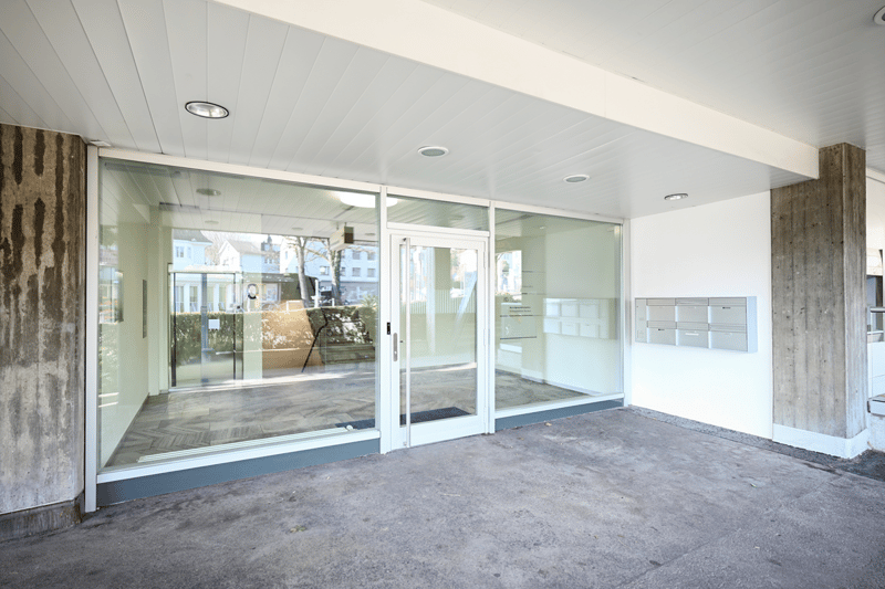 modern entryway with sliding and swinging doors, white ceiling and walls, large windows, mailboxes, grey concrete floor