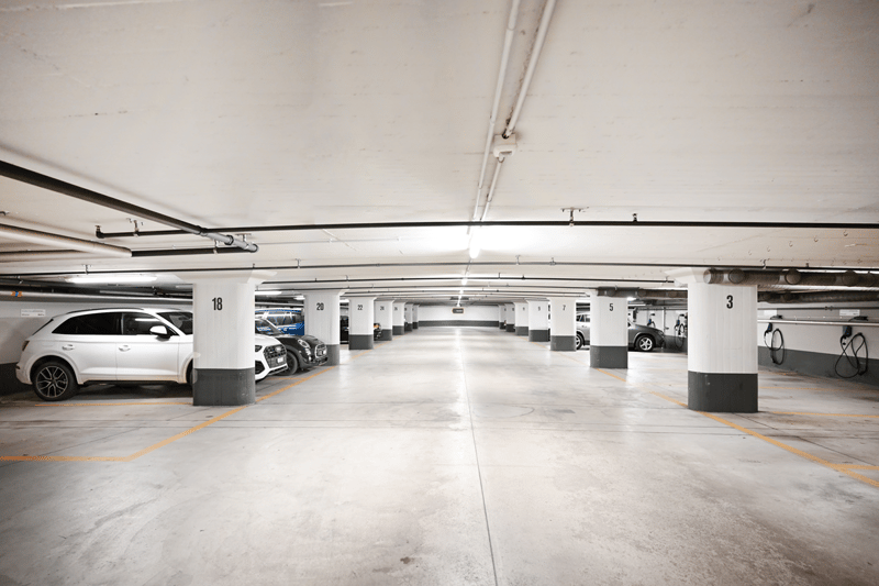 underground parking lot, 5 cars parked, electric vehicle chargers, grey ceiling, white pillars