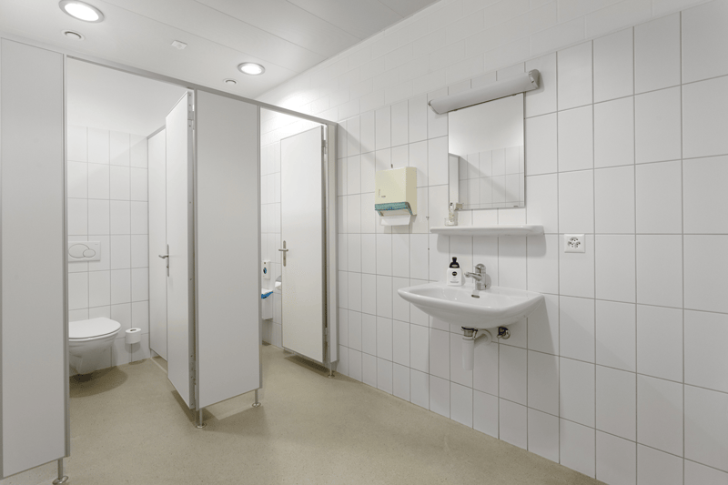 Small bathroom with white tile walls, a toilet in a partition, a sink with faucet, a mirror, and a tissue dispenser.