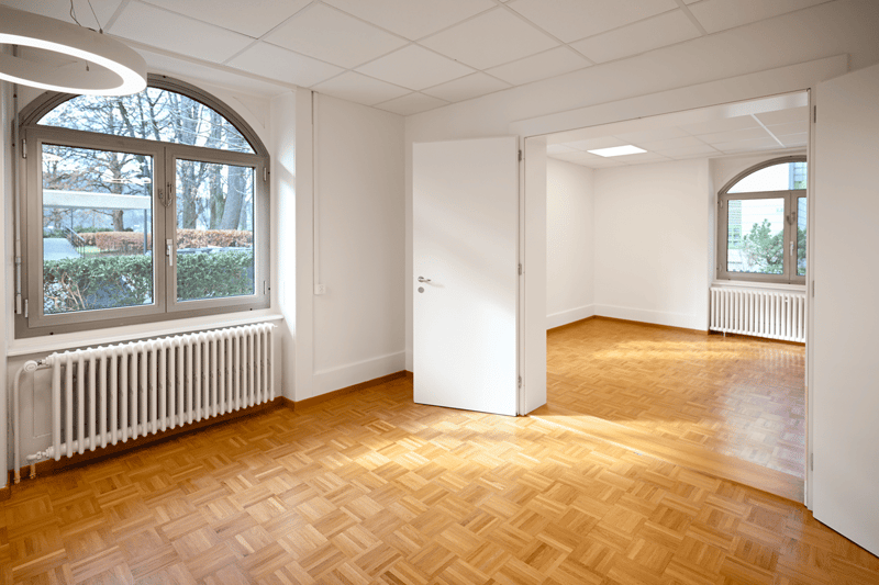 Wooden floor, two windows, two radiators, white walls, bright from the windows