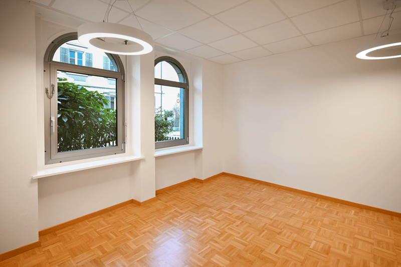 large room, wooden parquet flooring, white walls, circular lamps, arched windows with white frames, window sills
