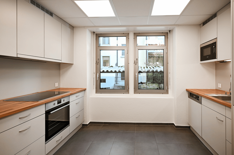 Contemporary style kitchen with white cabinets, tiled flooring, gas stove, oven, built-in microwave, stainless steel sink, wooden countertops