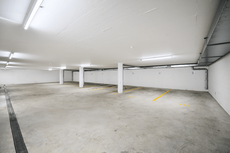 empty car park, white walls, concrete floor, several columns, several lights, parking spots