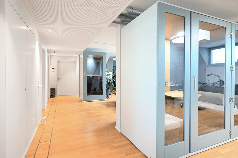 modern office hallway, wooden floor, white walls, glass doors, office booths, desk, plants