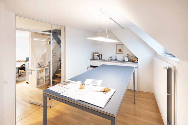 modern office room with glass door, table, radiator, kitchen area, wooden floor