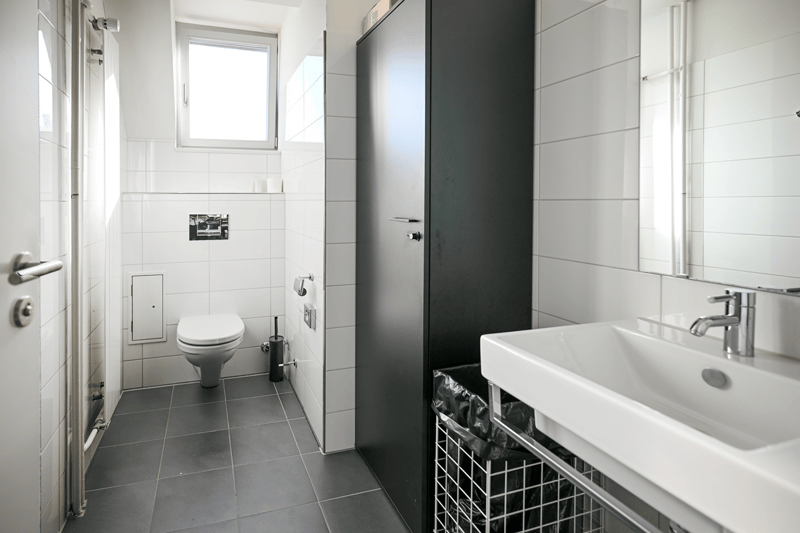 white tiles, white toilet, white sink, silver faucet, black trash bin, white mirror