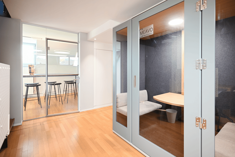 Office phone booth with glass walls, a small desk, and a bench.