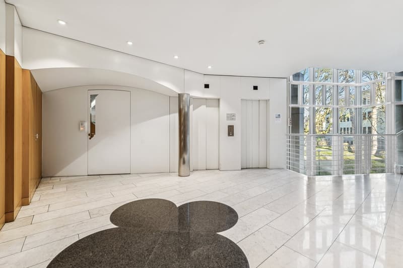White floors, white walls, glass windows, elevators, round grey tile mat
