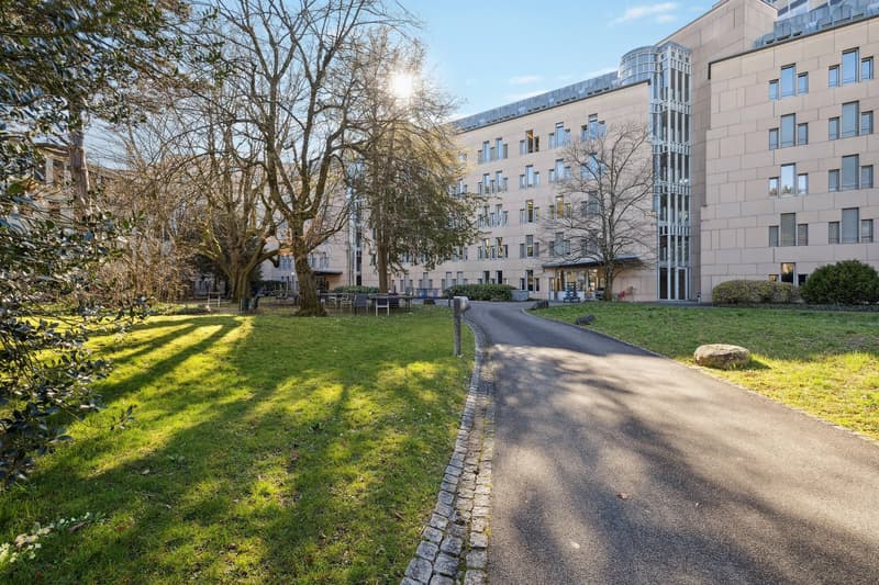 modern building, many windows, front garden with grass and trees, pathway leading to the entrance