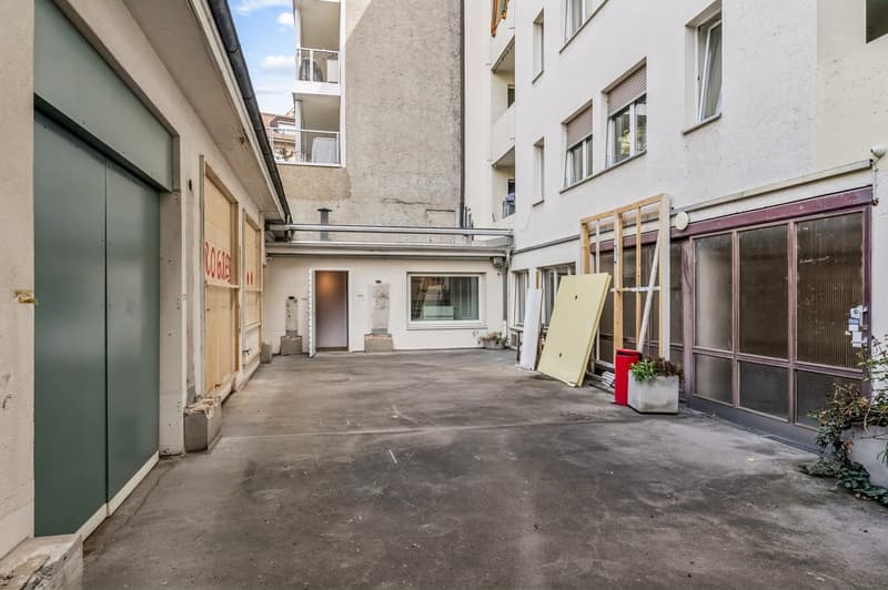 Empty parking lot, concrete floor, green doors, white walls, windows, potted plants, trash bin