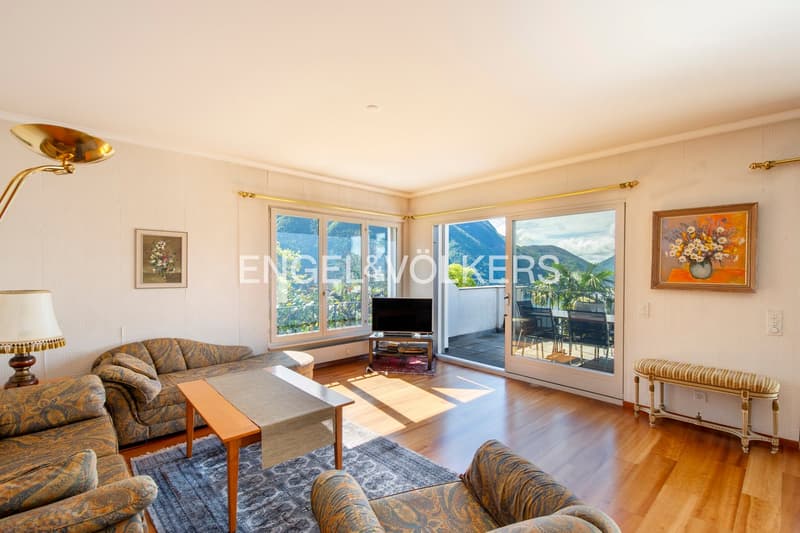 Spacious living room with large windows offering a scenic mountain view, hardwood floors, patterned upholstered sofas, wooden coffee table, and artwork on the walls