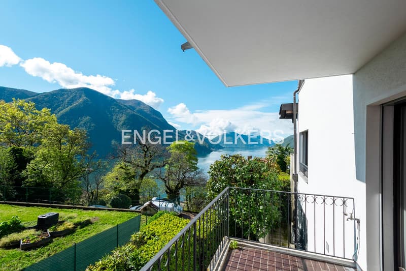 2-story house with a balcony overlooking a scenic lake surrounded by mountains and lush greenery