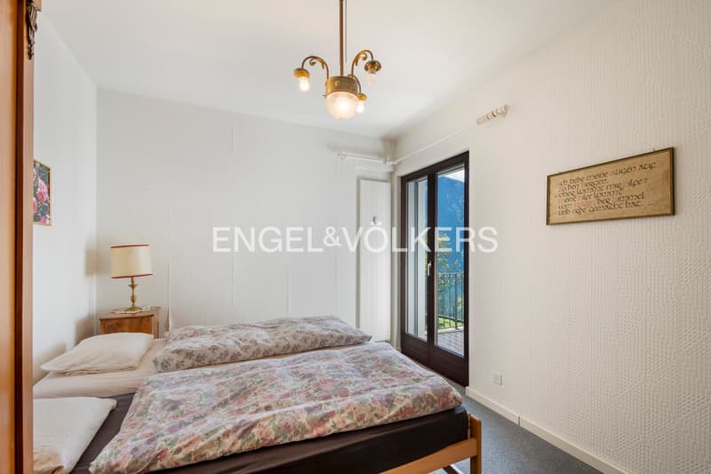 Spacious bedroom with large windows, floral bedding, wooden furniture, and a decorative wall hanging