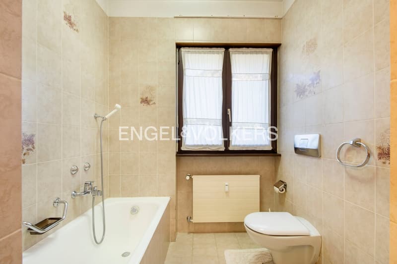 Tiled bathroom with bathtub, toilet, and window with curtains