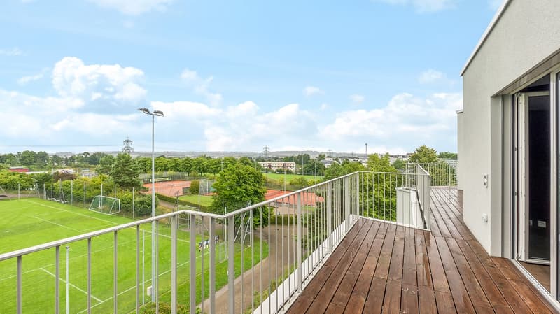 Terrace with large wooden deck, overlooking tennis court and green field, metal railing