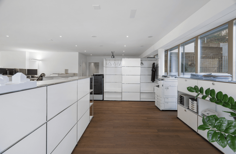 A modern office space with white walls, wooden floors, and glass windows.
