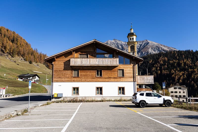 2 story wooden house, white lower floor, balcony, parking lot, bell tower, mountain view