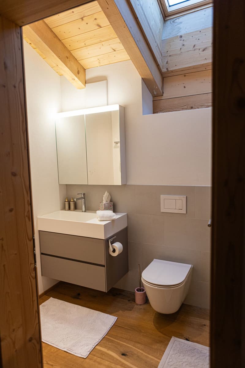 white sink, cabinet, mirror, toilet, bidet, wooden floor, white towels
