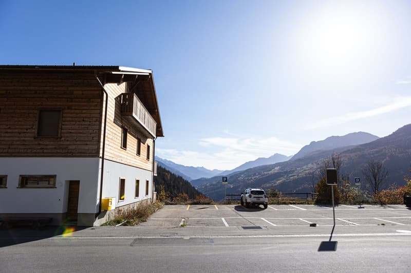 Modern house with wooden balcony, located in a mountainous area with a parking lot in front