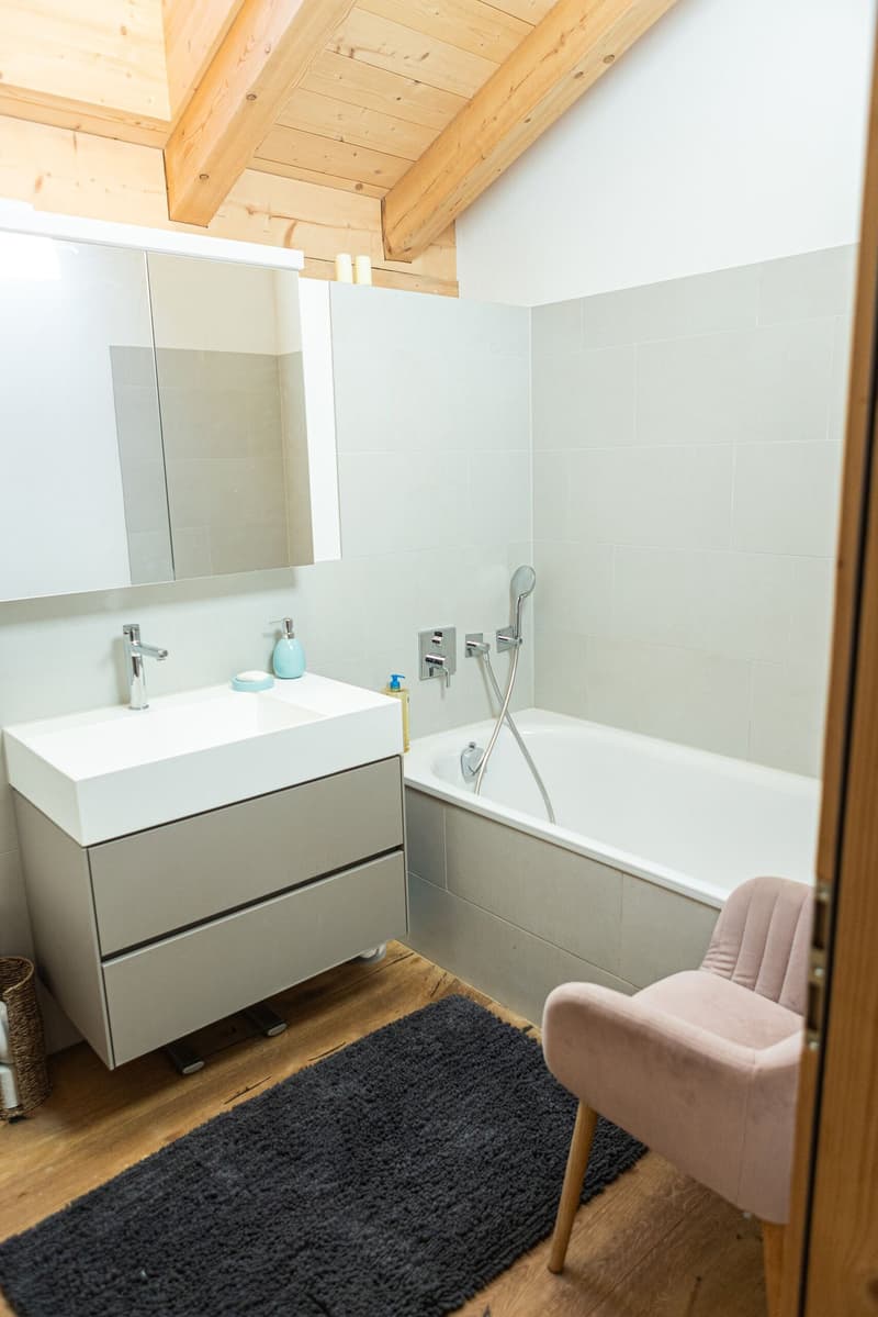 modern white bathroom with bathtub, sink, wooden floor, chair, mirror