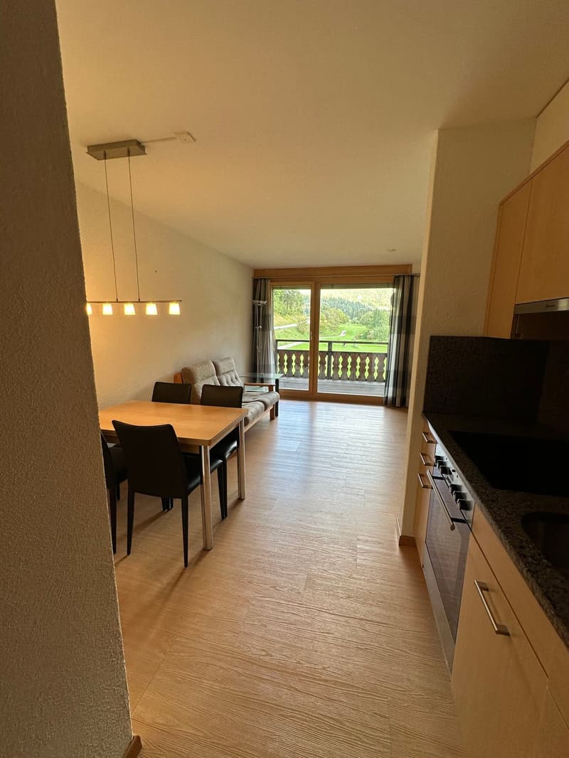 Dining room with table and chairs, couch, balcony, and kitchen area with stove and sink