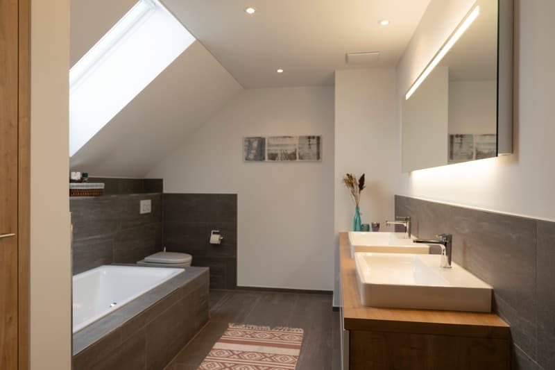 bathroom with bathtub, toilet, two sinks, mirror, skylight