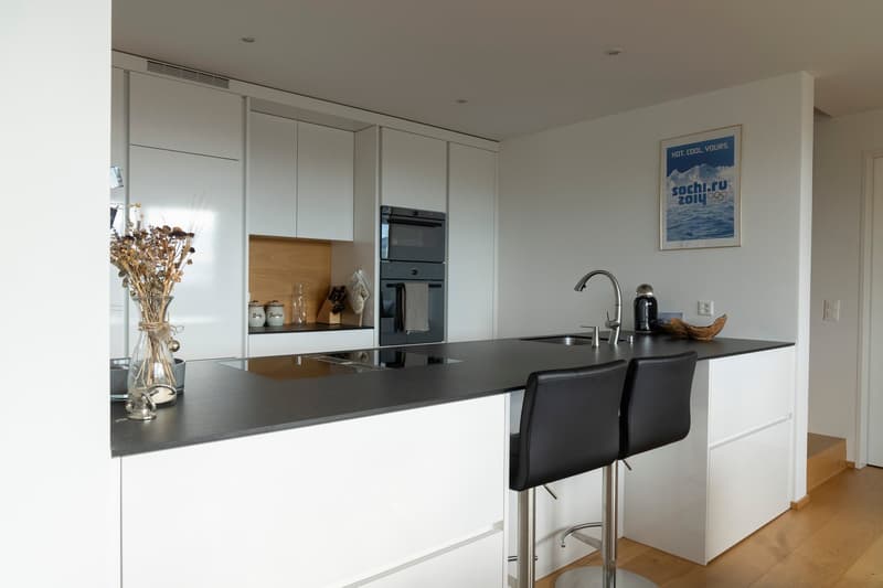 modern kitchen, white cabinets, black countertop, black bar stools, stainless steel appliances, wooden floor