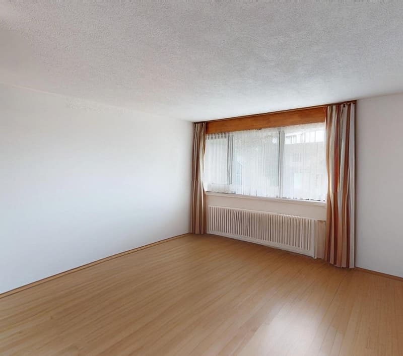 an empty room with a window, wooden floor, white walls and a radiator