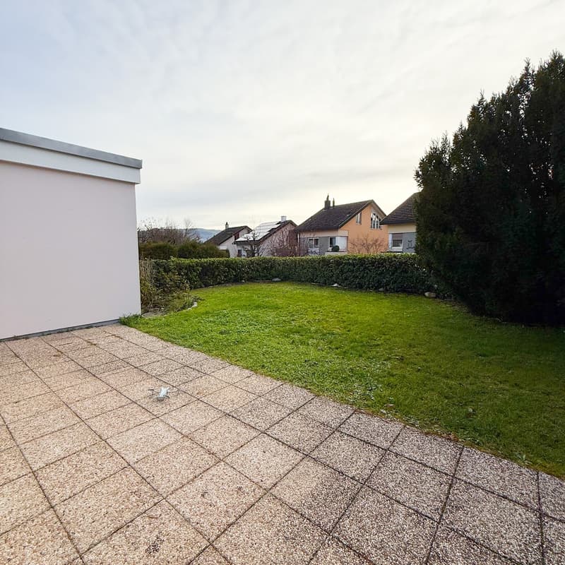 Green lawn, hedge, gravel path, white house side, clear sky