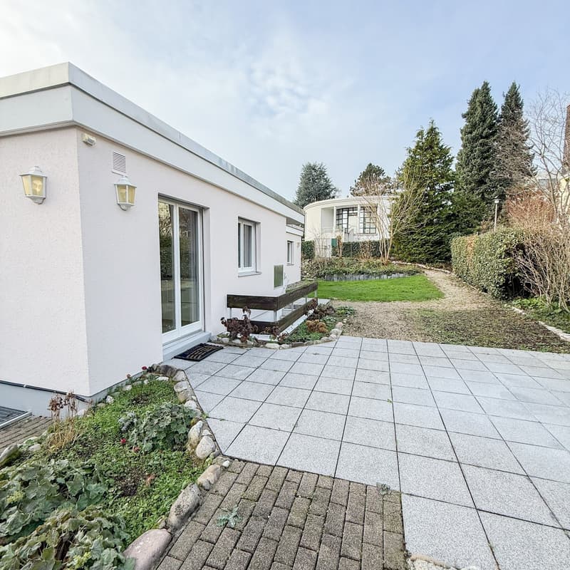 White modern house with double glass door, two lamps on the left side, brick pathway, green lawn, and plants.