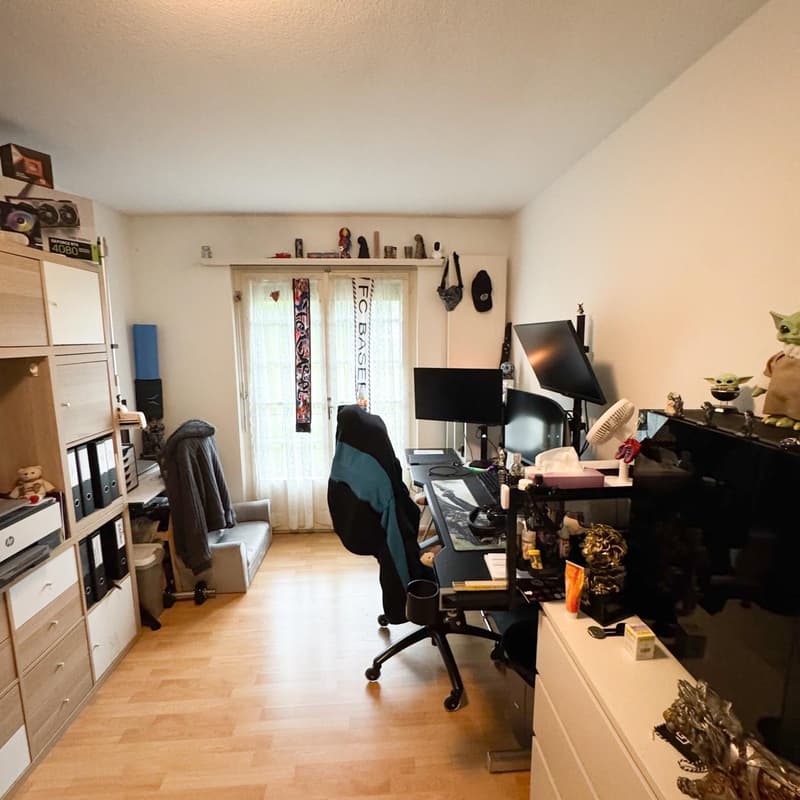 A room contains an office chair, desk, monitor, figurines, and a bag. On the left side, there is a couch, storage box, shelf, file folders, books, and a teddy bear. On the right side, there is a baby Yoda doll, a black TV, a bottle, a box, and a fan. A wh