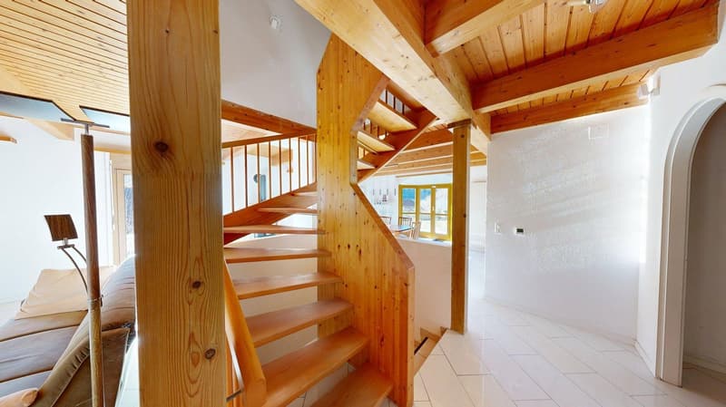 Entrance hall with wooden stairs, white tiles, wooden ceiling beams, large windows, couch with pillows