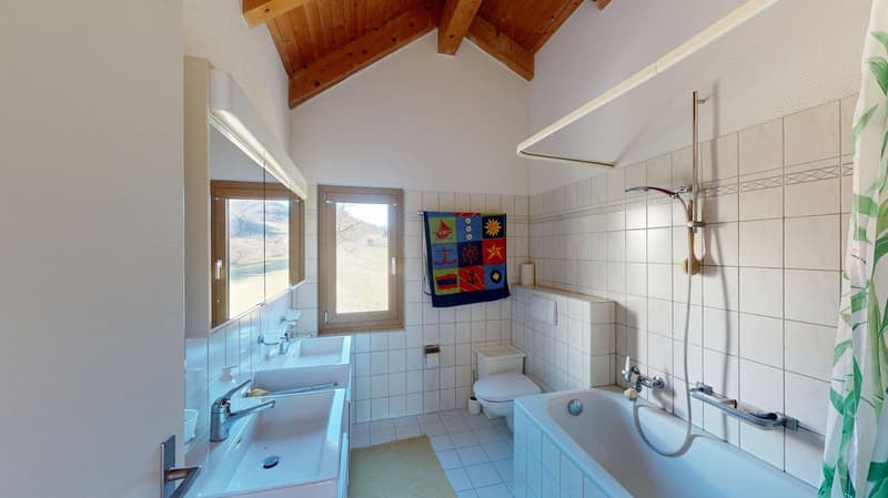 White tiled bathroom with wooden ceiling, two sinks, bathtub, toilet, towel hanging, mirror, shower