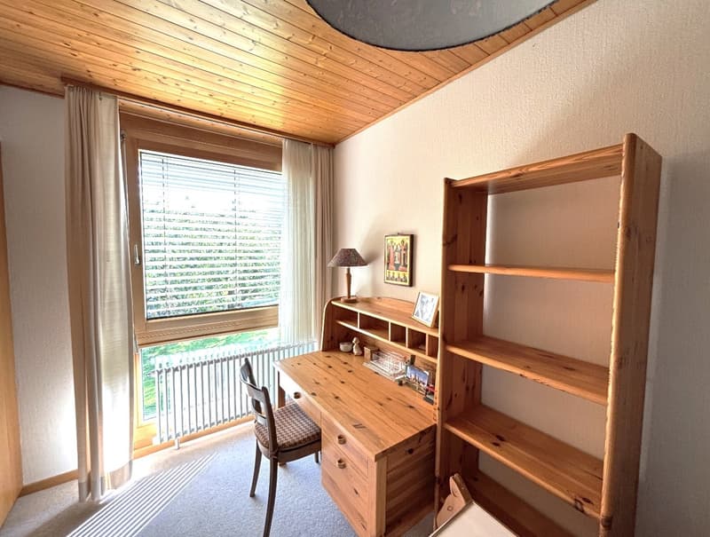 desk with drawers, wooden chair, large window with blinds, picture frame on the desk, wooden shelves, lamp on the desk