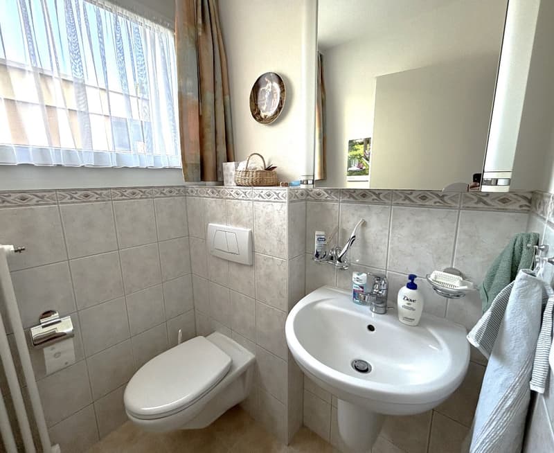 bathroom with tile wall, white toilet, white sink, mirror, basket on top of wall
